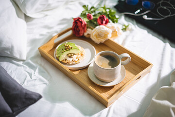 Tray with cup of coffee and light sandwich in a bed with Laptop on the background, morning light