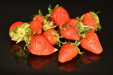 Bright red ripe strawberries with green ponytail, close-up, on a black background.