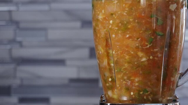 cooking healthy fresh mexican hot salsa in a glass blender, blending boiled tomato, onion, jalapeno cilantro and garlic