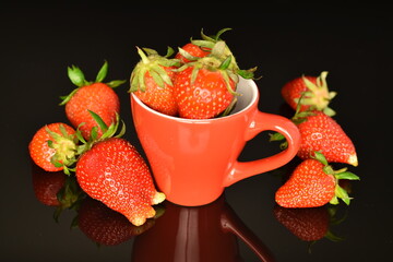 Several sweet strawberries with a red ceramic cup, close-up, on a black background.
