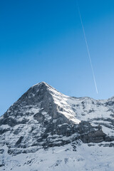 Amazing Peak of a Majestic, rocky and High Snowy Mountain in a Sunny Day in Switzerland with an Airplane Contrail