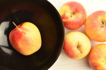 Several ripe organic, juicy, aromatic apples in a black ceramic plate, close-up, on a painted wooden table.