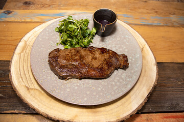 A delicious tender tenderloin steak on a plate with a a pot of red wine sauce and garnish on a wooden kitchen table
