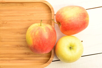 Three ripe organic, juicy, fragrant apples on a bamboo tray, close-up, on a painted wooden table.
