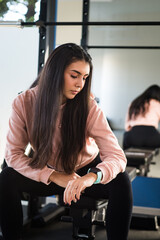 Fototapeta na wymiar Beautiful girl sitting looking at the time waiting to start training in the gym with her personal trainer. ..