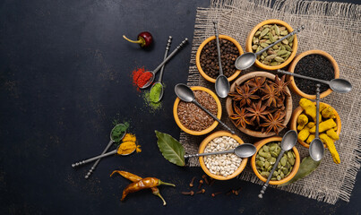 Fototapeta na wymiar Spices and condiments in spoons and bowls for cooking on black background