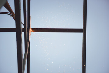 Young man worker welding iron pieces at work with protective goggles. Building construction concept.