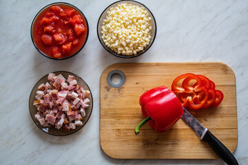 Cooking at home concept: cutting board, knife, bacon, red peppers, tomatoes and cheese