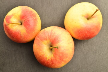 Three ripe organic, juicy, aromatic apples, close-up, on a slate serving plate.