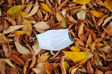 coronavirus COVID-19 pandemic. antiviral medical mask for protection against corona virus. Surgical protective mask. Used and left on autumn leaves