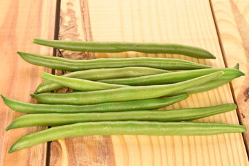 A few pods of bright green, organic, natural, ripe beans, close-up, on a wooden table.