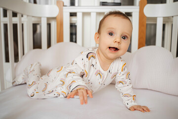 Happy baby smile on bed in baby's room. Adorable infant in stylish pajama lying on   comfortable cot at home.