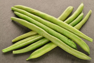 A few pods of bright green, organic, natural, ripe beans on a serving plate of slate.
