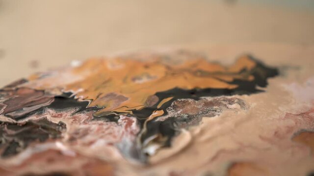 Closeup artist is drying beige black brown picture with drainer. Process of drawing, making abstract liquid acrylic painting. Tools for creating effects waves on canvas. Fluid art therapy concept.
