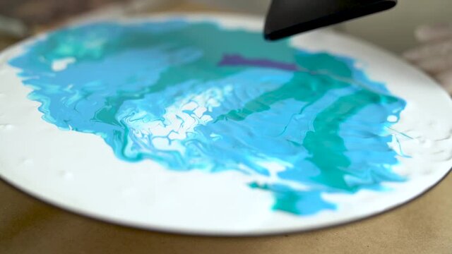 Closeup artist is drying blue green white picture with drainer. Process of drawing, making abstract liquid acrylic painting. Tools for creating effects waves on canvas. Fluid art therapy concept.