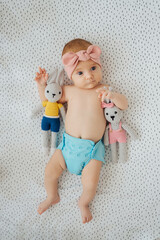 Cute infant in reusable diaper and stylish headband with toy bunny lying  on bed at home. Baby with...