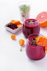 Smoothie with beet root, berries and blood orange topped with microgreen in a glass on white