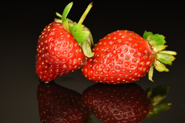 Two bright red ripe organic delicious strawberries. The background is black.
