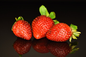 Bright red ripe strawberries with green ponytail, close-up, on a black background.
