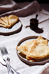 Traditional Russian crepes or pancakes on gray plates over greige linen tablecloth. Pancake week or Shrovetide