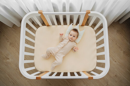 Top view of adorable infant in stylish pajama lying on pillow crown in comfortable cot at home. Baby in cradle