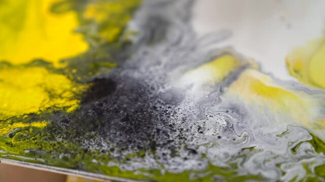 Closeup splashes of alcohol appearing on canvas. Creation of ornament on white yellow black picture. Process of drawing, creating abstract liquid acrylic painting in workshop. Fluid art therapy.