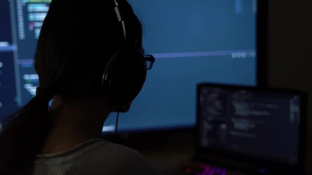 Software developer freelancer woman female in glasses work with program code C ++, Java, JavaScript on multiple displays on workplace at night. Programmer girl develops web desktop mobile application.