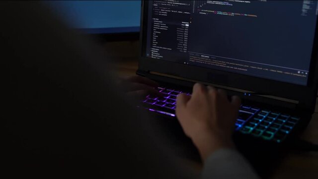 Closeup female hands is typing on laptop keyboard with colored backlight. Software developer freelancer woman work with program code on workplace at night. Programmer girl develops web application.