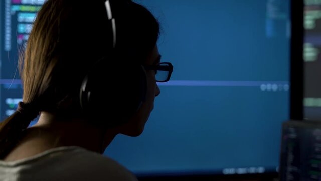 Software developer freelancer woman female in glasses work with program code C ++, Java, JavaScript on multiple displays on workplace at night. Programmer girl develops web desktop mobile application.