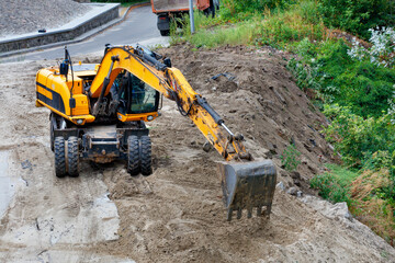 Heavy construction excavator works at a construction site among the near asphalt road.