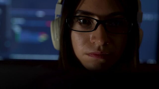 Portrait of software developer freelancer woman female in glasses work with program code on laptop at workplace at night. Programmer girl develops web desktop mobile application. Projector background.