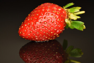 One red appetizing strawberry, close-up, on a black background.