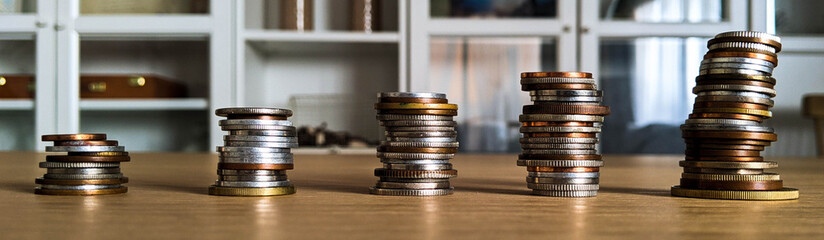 Save money concept. Stack of coins at home on a wooden table and a bookshelf in the background