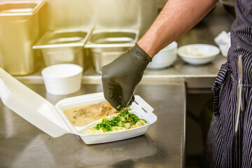 Chef preparing dish to a box in the restaurant for food delivery service to home, online ordering