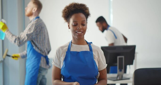 Portrait of african female janitor putting on gloves working in office