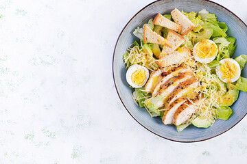 Caesar salad with lettuce, chicken, avocado and croutons on light table. Top view, above, copy space
