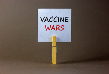 COVID-19 vaccine wars symbol. White paper with text 'vaccine wars', clip on wood clothespin. Beautiful grey background. COVID-19 vaccine wars concept.