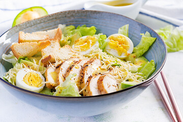 Caesar salad with lettuce, chicken, avocado and croutons on light table.