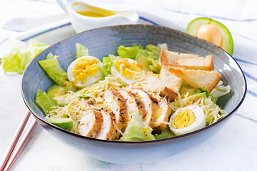 Caesar salad with lettuce, chicken, avocado and croutons on light table.