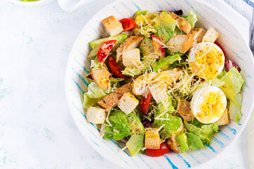 Caesar salad with lettuce, chicken, avocado, cherry tomatoes and croutons on light table. Top view, above, copy space