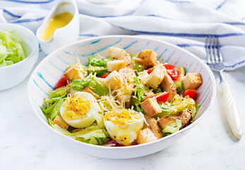 Caesar salad with lettuce, chicken, avocado, cherry tomatoes and croutons on light table.