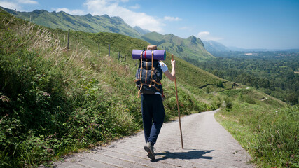 Caminante de peregrino con mochila, sombrero de paja y palo de madera por camino entre montañas en...