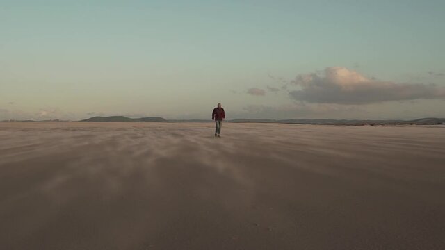 Man walking on sandy beach at sundown