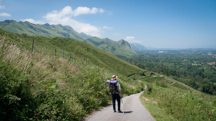Caminante de peregrino con mochila, sombrero de paja y palo de madera por camino entre montañas en...