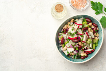Vegetable salad with radish, celery, red onion, beans and greens in bowl on concrete background