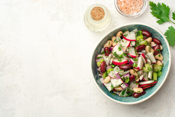 Fototapeta na wymiar Vegetable salad with radish, celery, red onion, beans and greens in bowl on concrete background