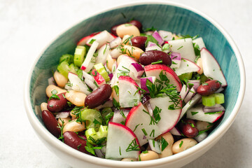 Vegetable salad with radish, celery, red onion, beans and greens in bowl on concrete background