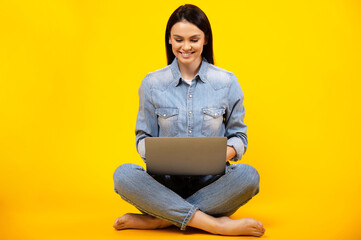 Beautiful young caucasian smiling woman in casual denim outfit, sitting on isolated orange...