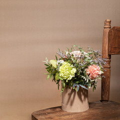 Flowers bouquet in ecological DIY cardboard vase standing on old wooden chair on beige with shadows...