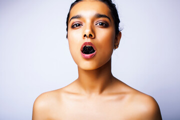 young pretty indian woman with dry fruit in mouth on white background